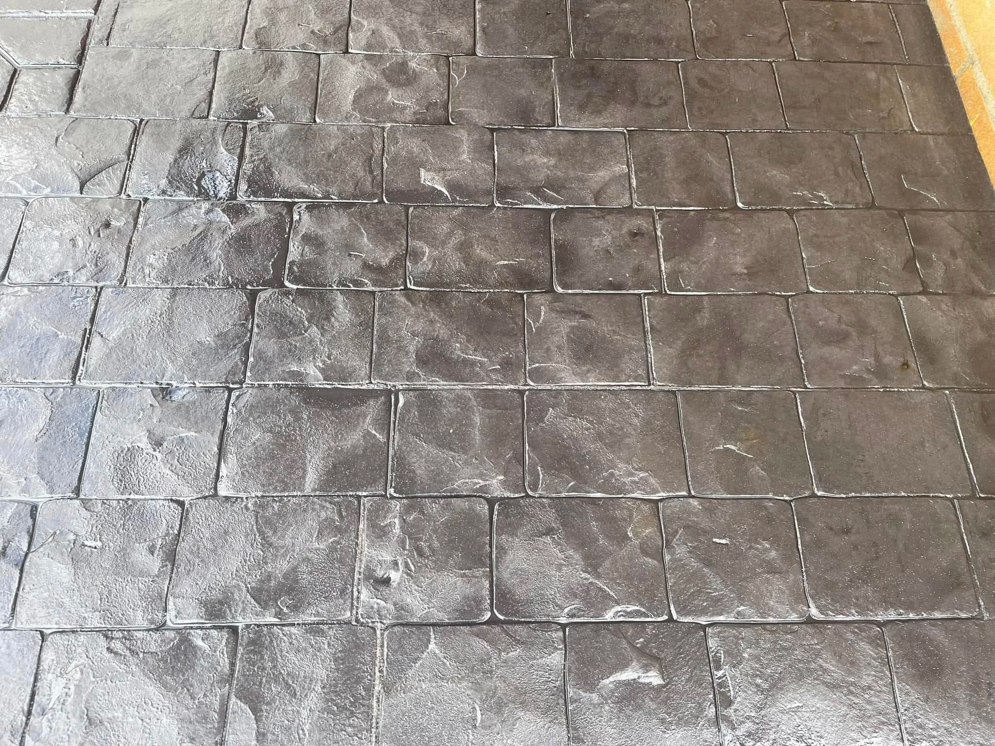 Close up of charcoal imprinted concrete stamped in a cobble setts pattern, showing the riven surface texture and pale grey release agent highlights in the joints