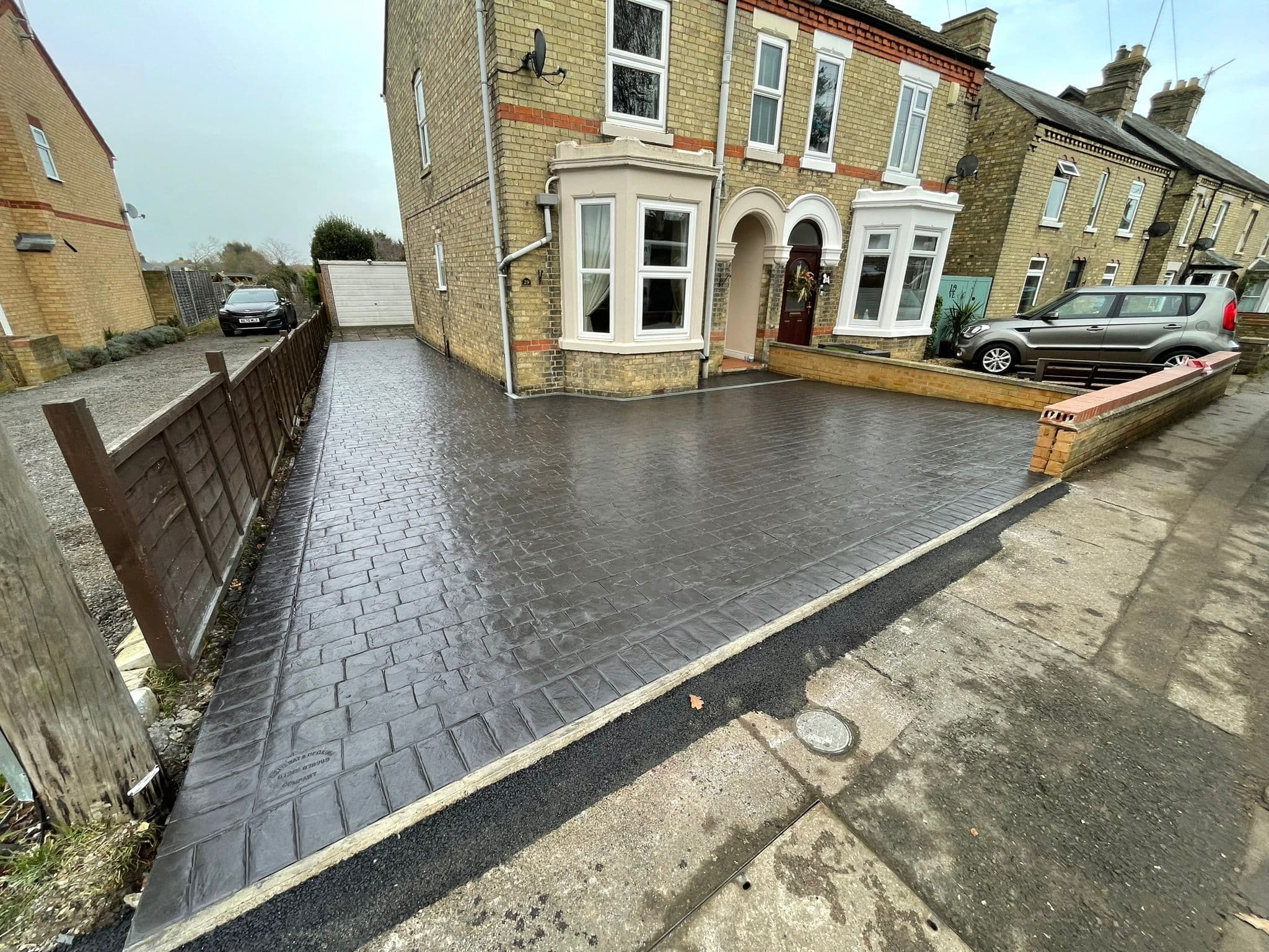 Charcoal imprinted concrete driveway stamped in a London cobble pattern in front of a yellow brick house