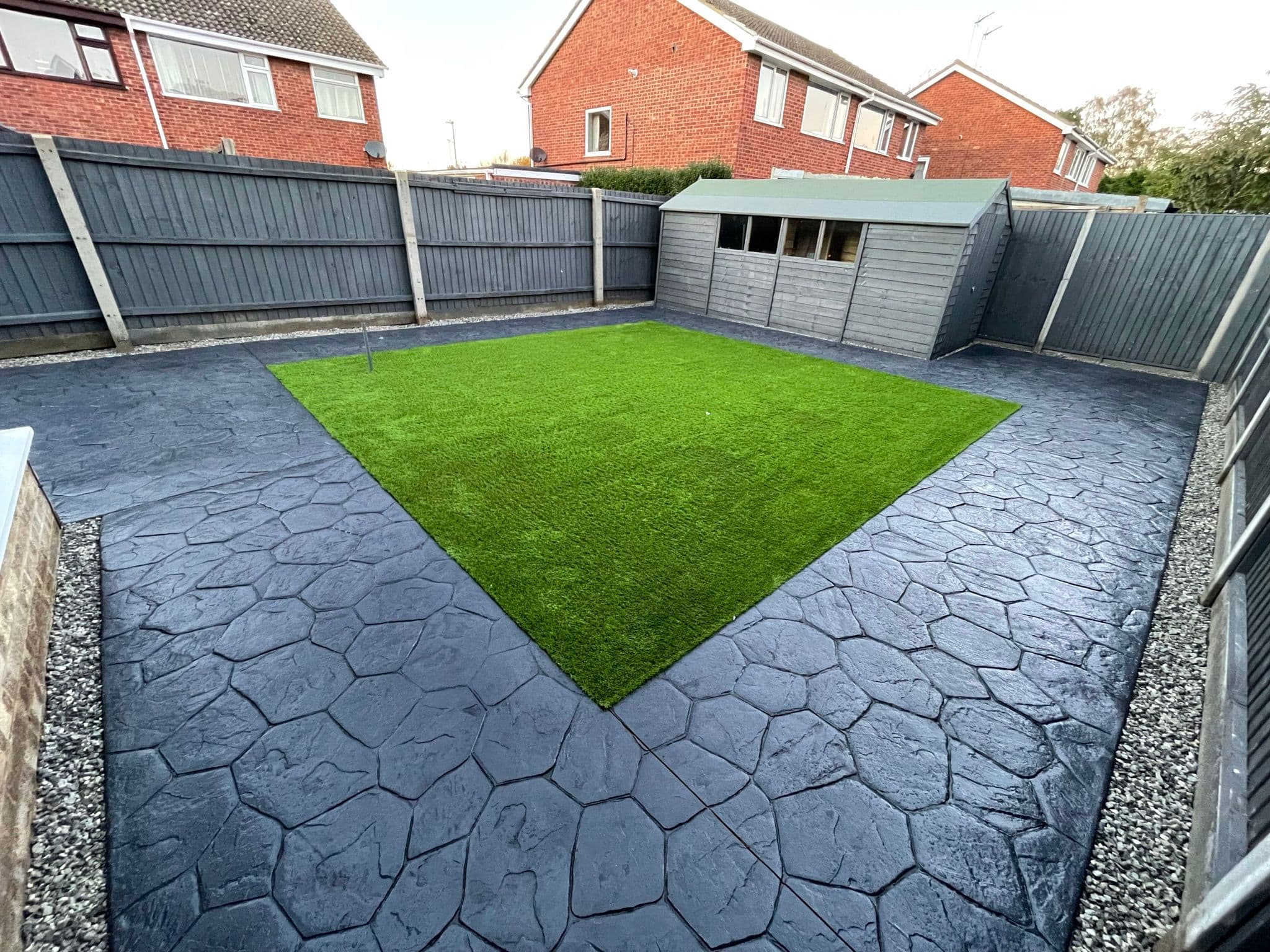Dark charcoal imprinted concrete stamped in an irregular random stone pattern around a rectangular artificial turf panel